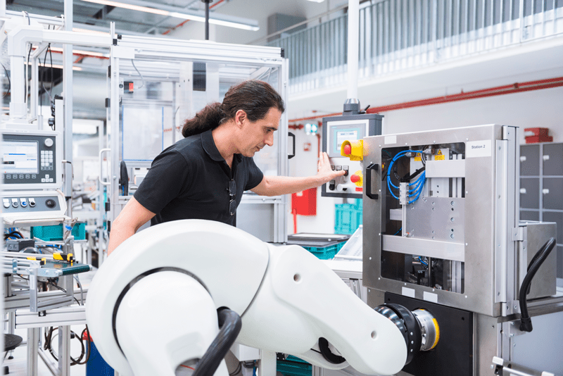 Ingenieur bedient resistiven Touchscreen an Industrieanlage mit Roboterarm
