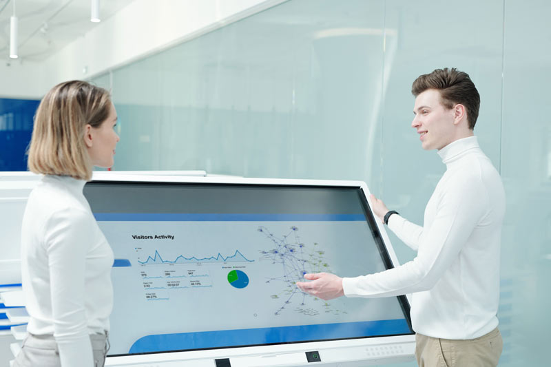 Zwei Personen analysieren Daten auf einem kapazitiven Touchscreen im Büro
